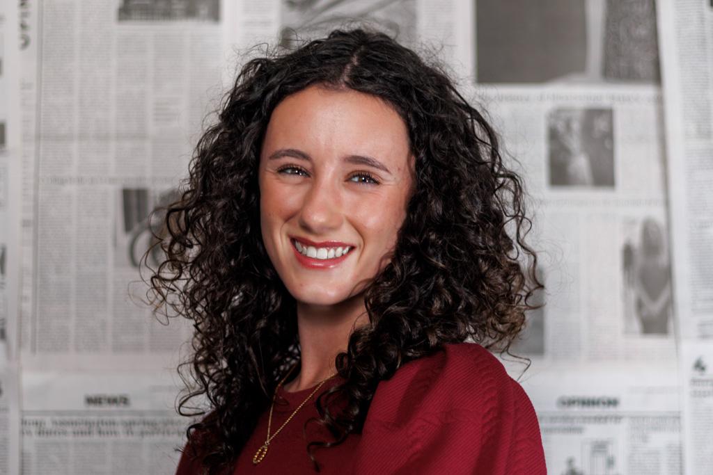 Casual photo of Kate Myers standing in front of newspapers